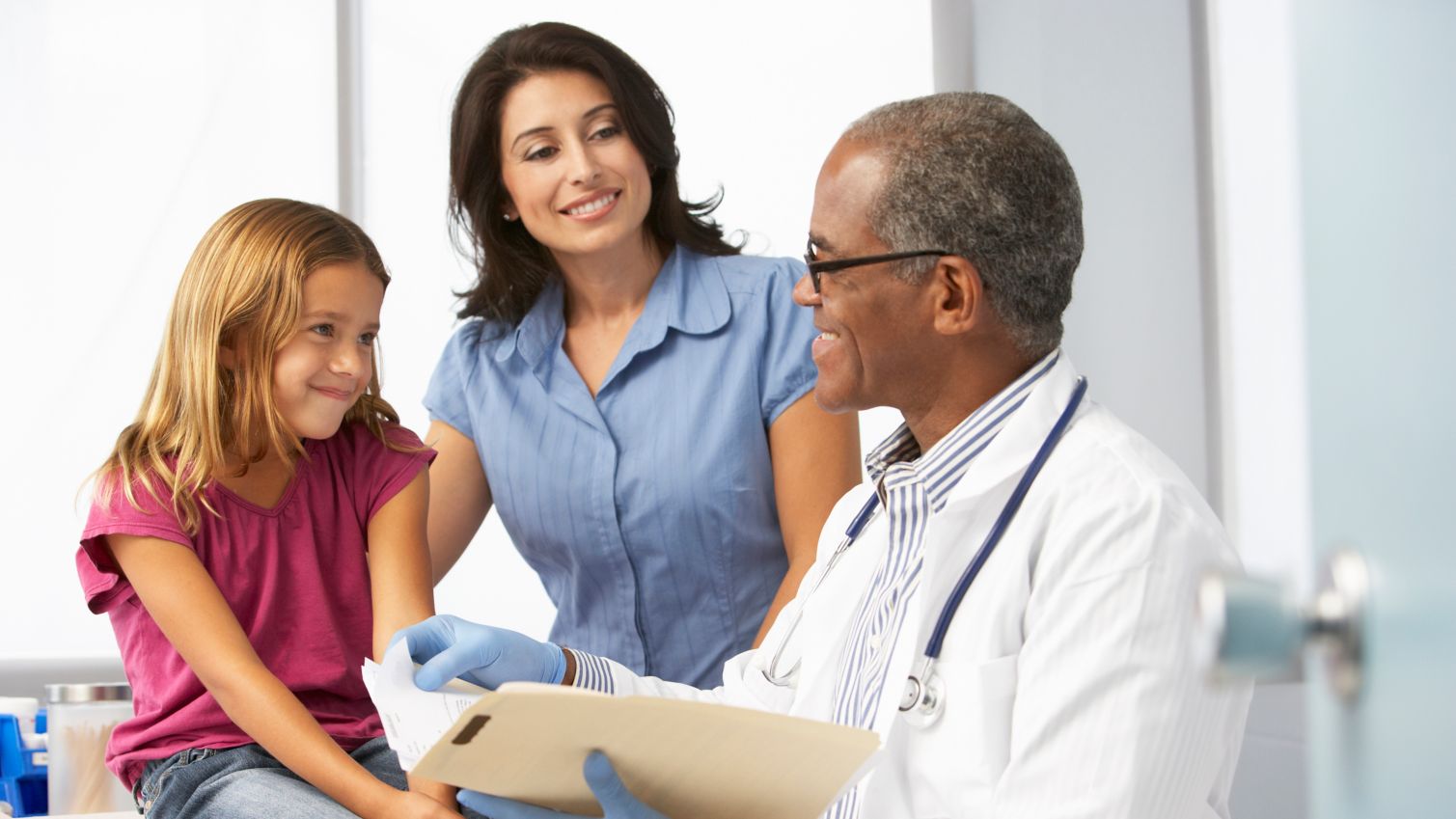 A physician talks to a young girl and her mother in an office