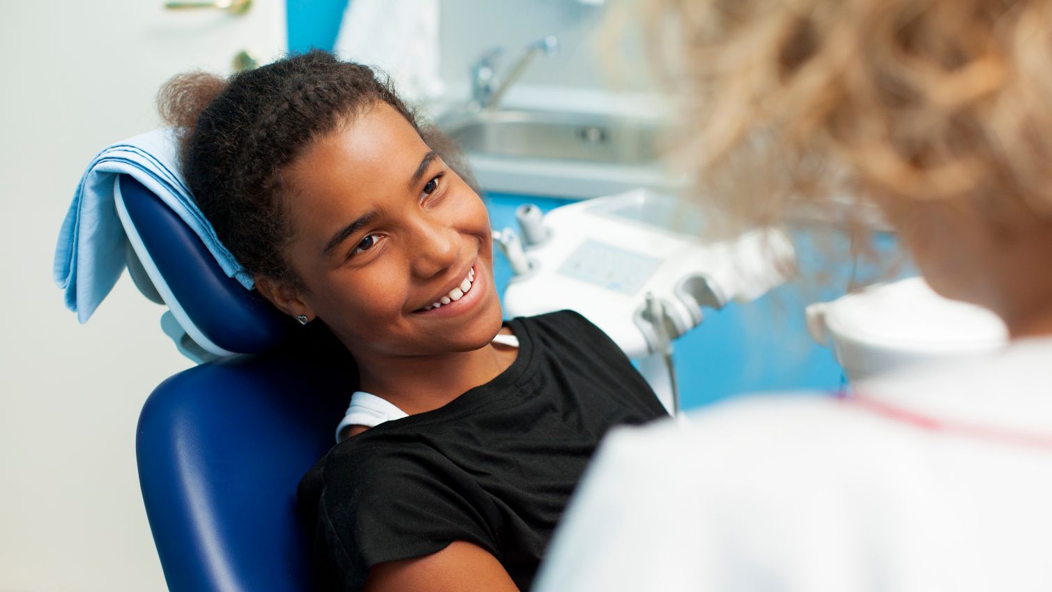 Child smiles as she listens to a dental healthcare provider.