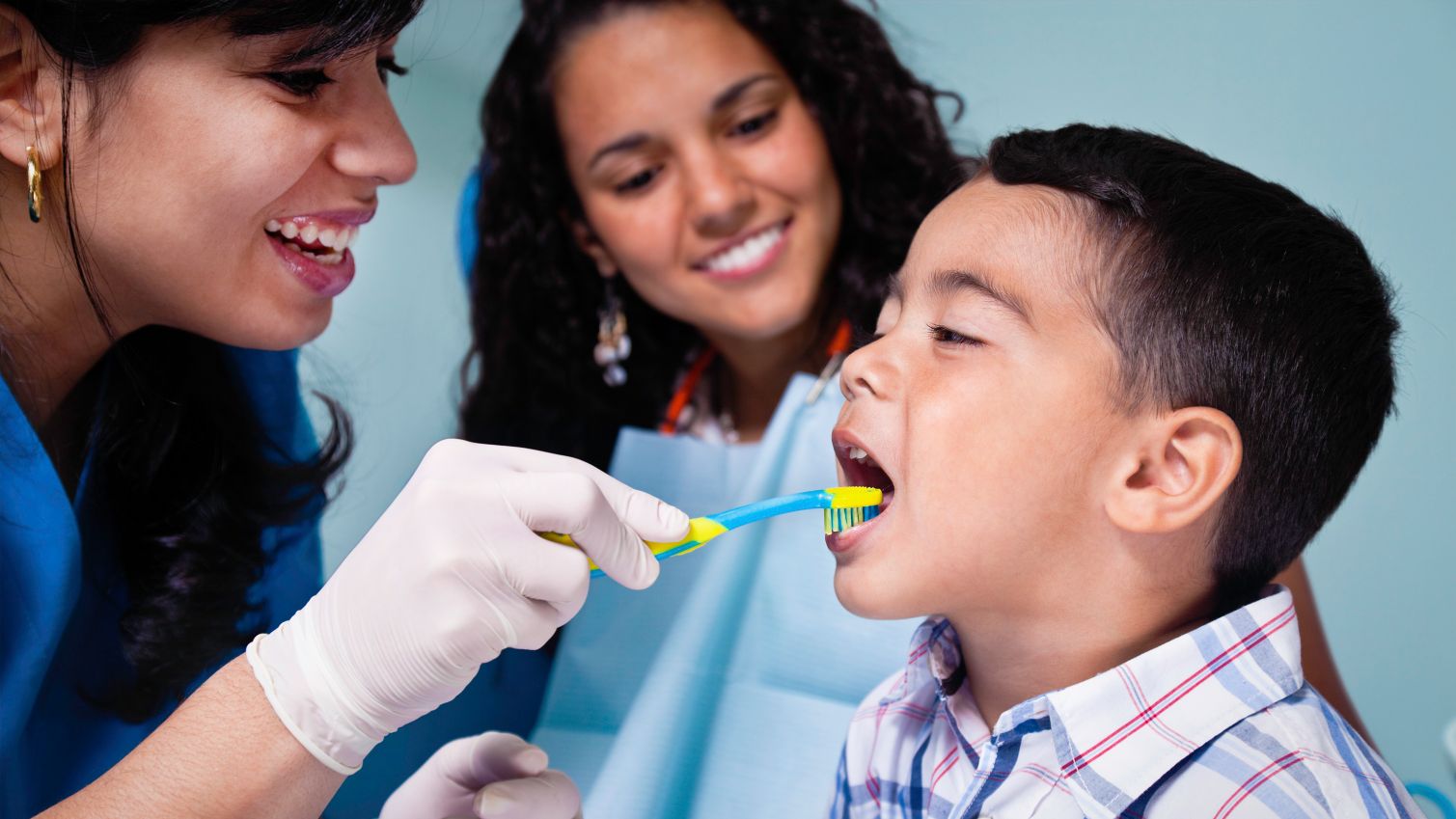 Dentist brushes boy’s teeth while mom watches