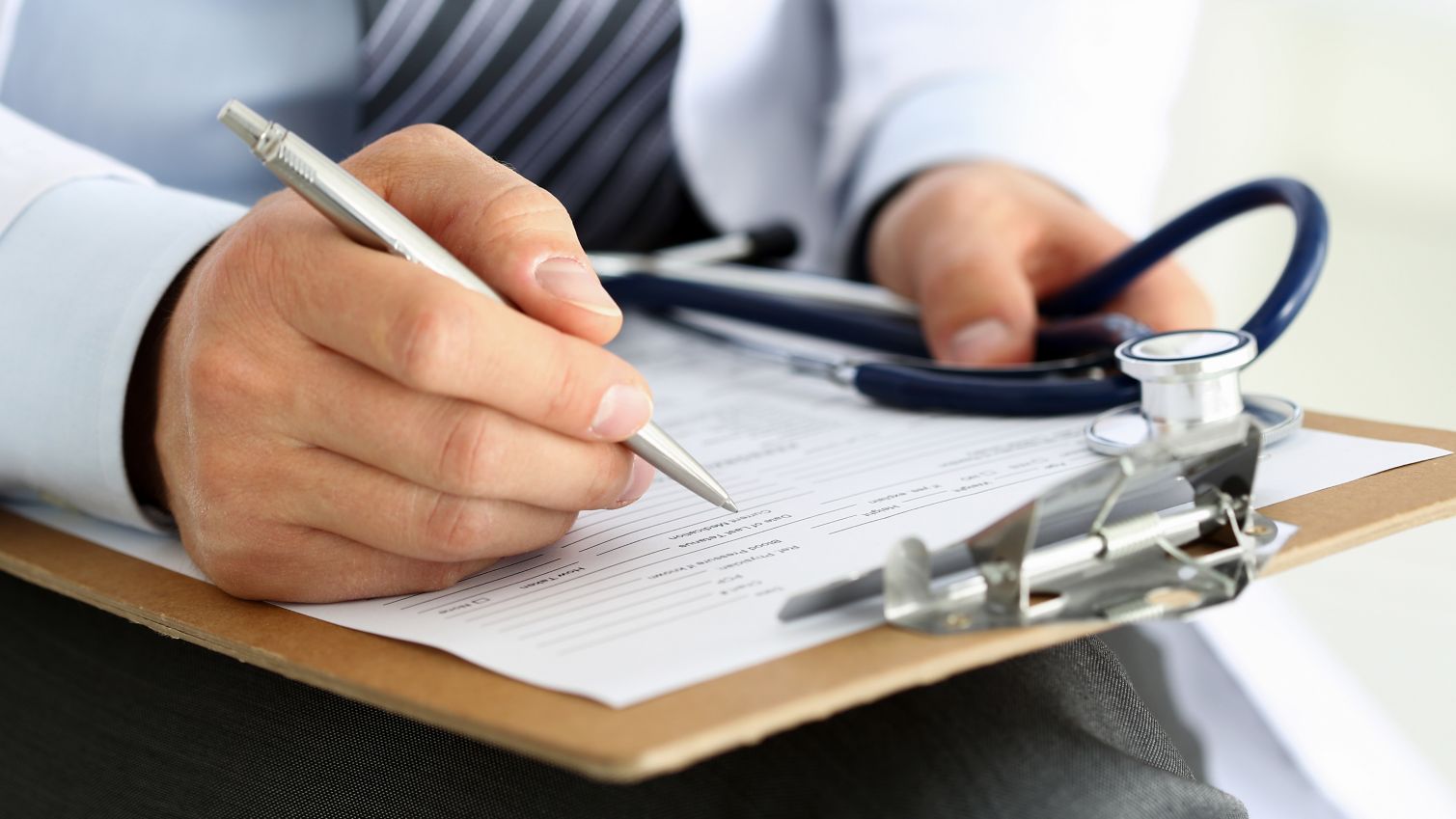 A closeup of physician's hand writing on a clipboard