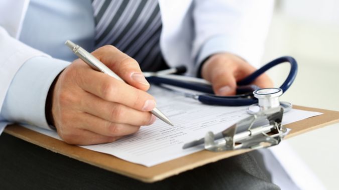 A closeup of physician's hand writing on a clipboard