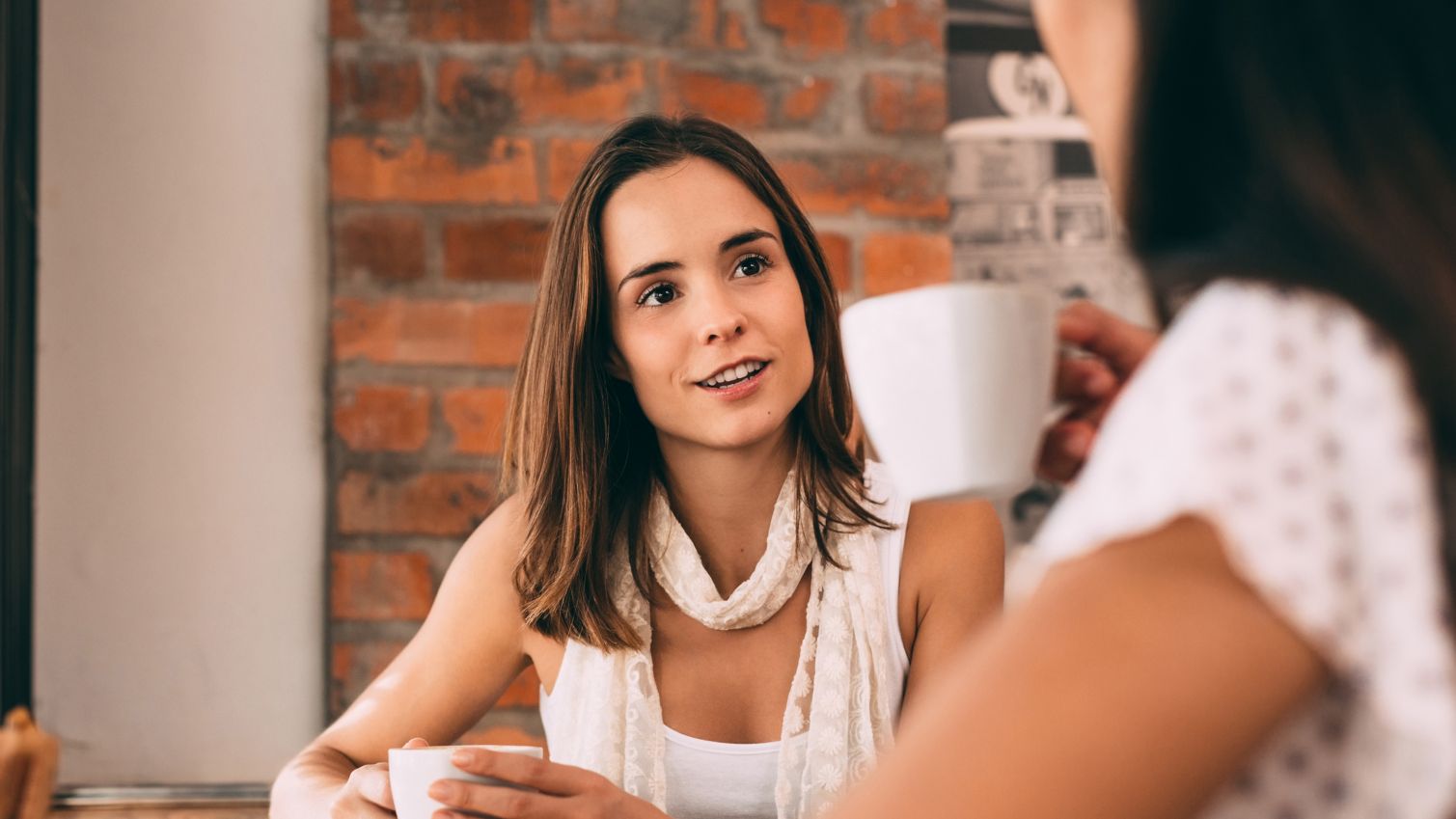 Young woman holds a tea cup as she talks to another woman at a cafe