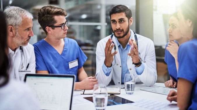 A physician holds up his hands while chatting with a group of his peers