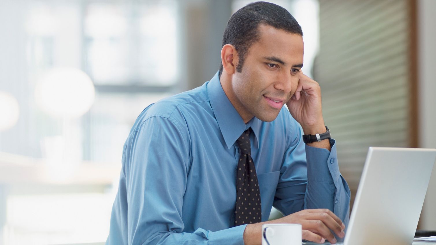 A man dressed in business attire works on a laptop