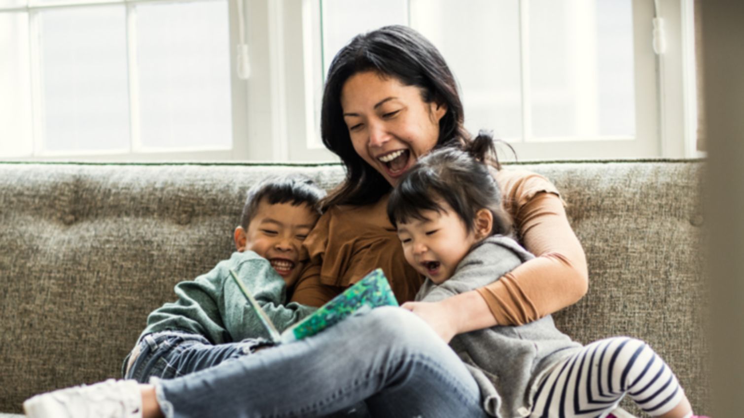 A mom and her 2 young children share a laugh, as she reads them a book.