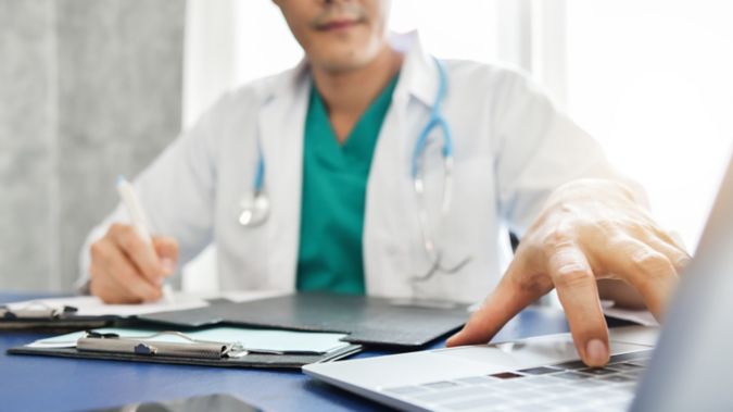 A physician reaches for his laptop while working on a patient's chart