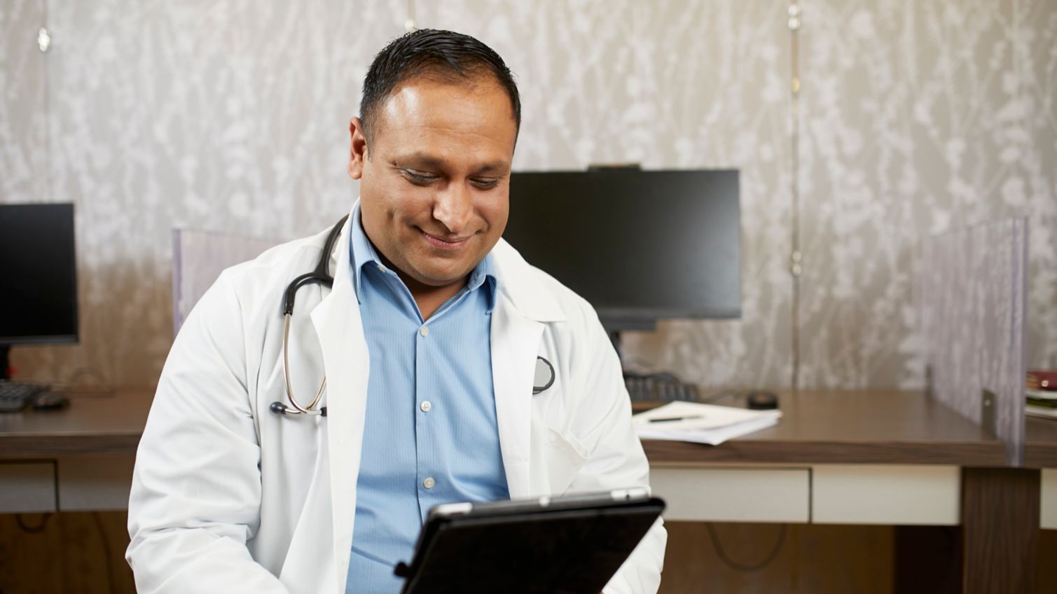 A smiling physician looks at information on his tablet