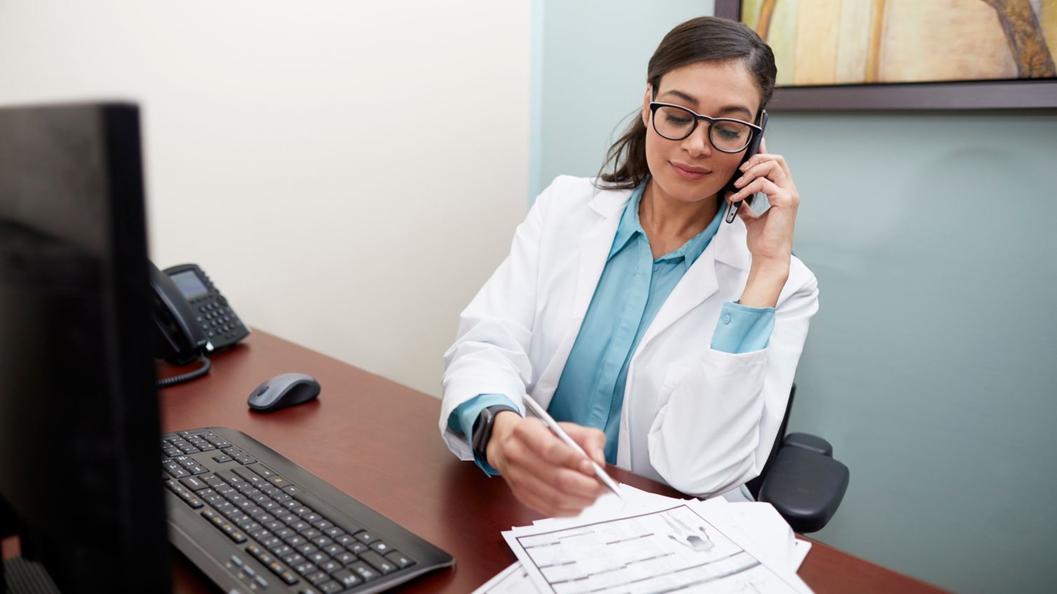 A physician takes notes while on her phone