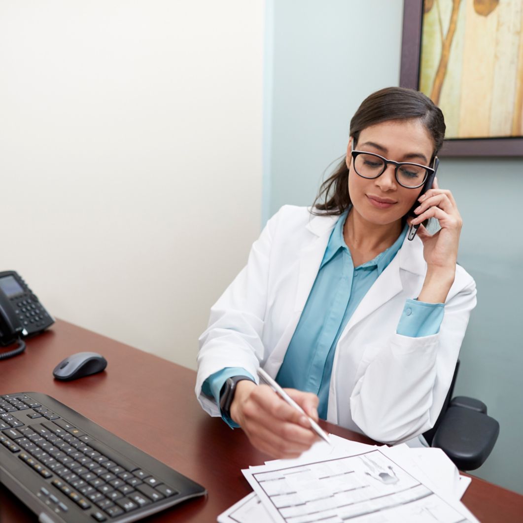 A physician takes notes while on her phone