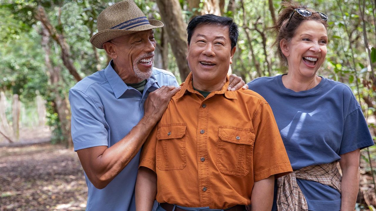 Two adult men and one adult woman smiling in a park setting