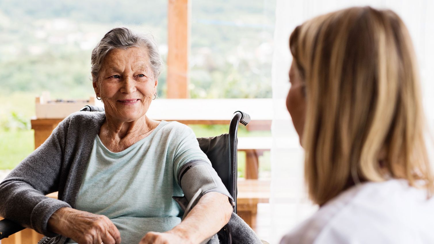 Older woman in wheelchair talking to female nurse.