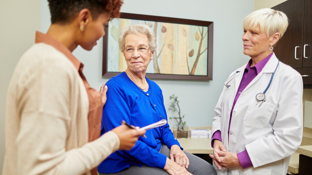 Older white woman in medical office with doctor and nurse