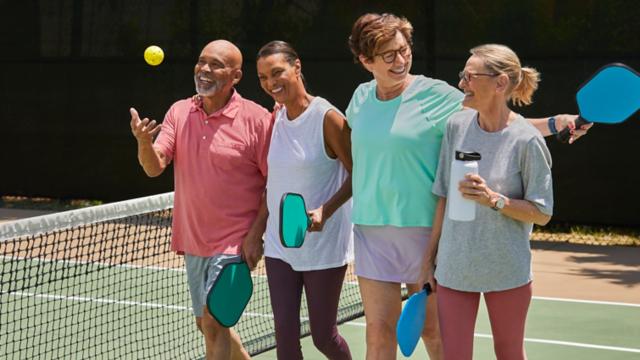 A group of friends walk onto a pickleball court together. 