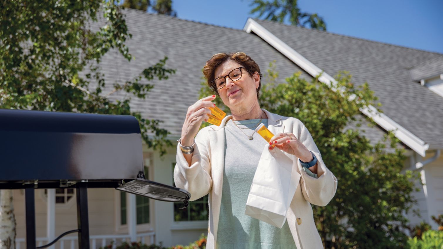 A woman stands at her mailbox and reads the labels on prescription bottles she's pulled from a package.