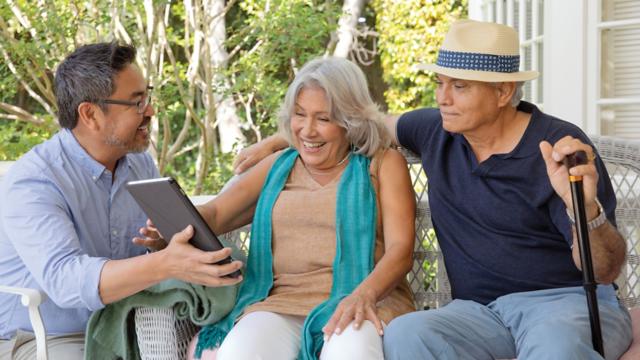 A couple sits on their porch with an agent while looking at a tablet.
