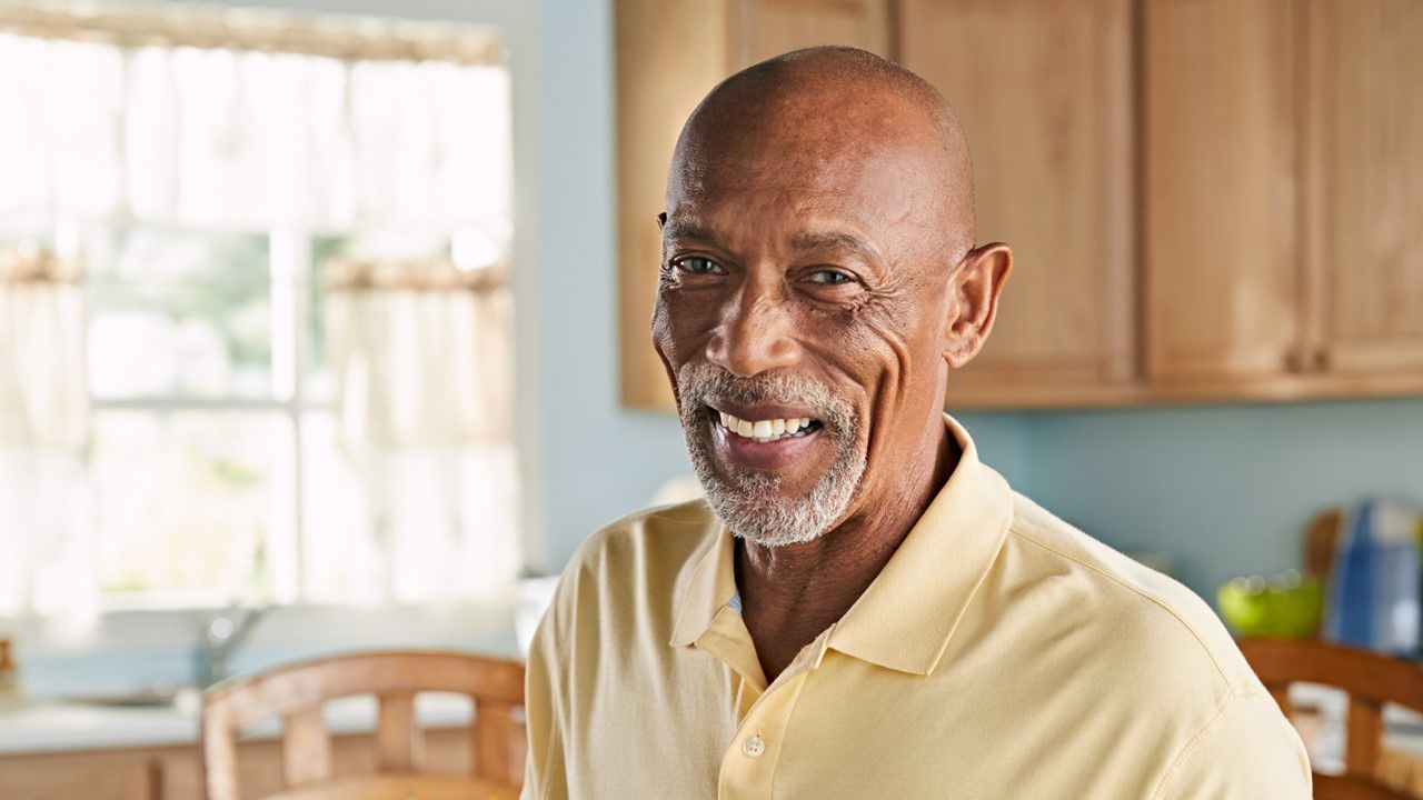 African American man wearing yellow shirt smiling in his kitchen