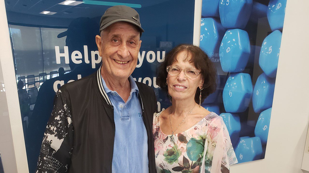 Two people smiling and standing in front of a blue sign