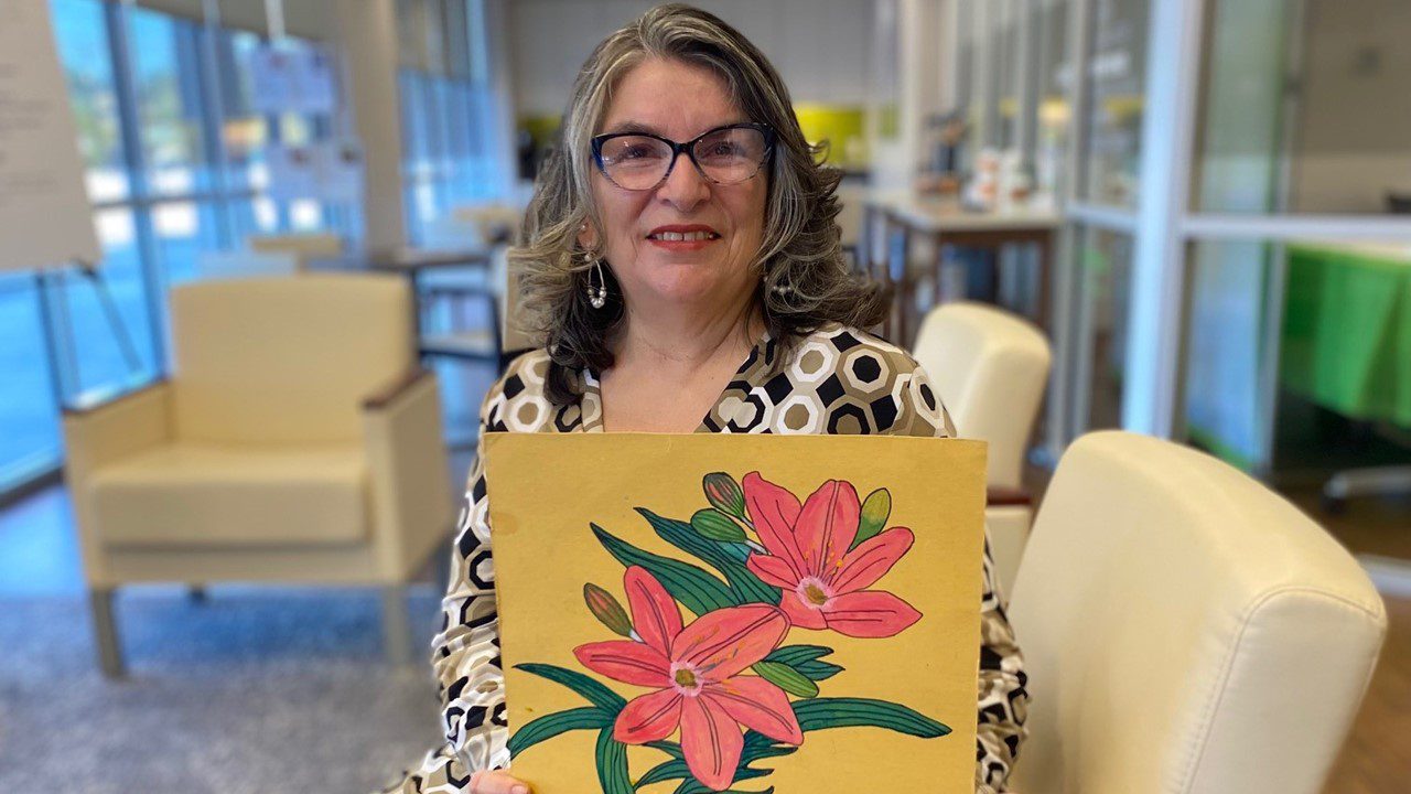 Woman holding her artwork of pink flowers with yellow background