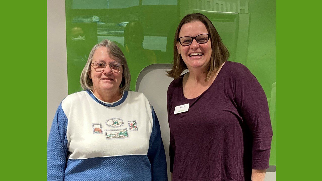 Two women smiling and standing in front of Humana sign