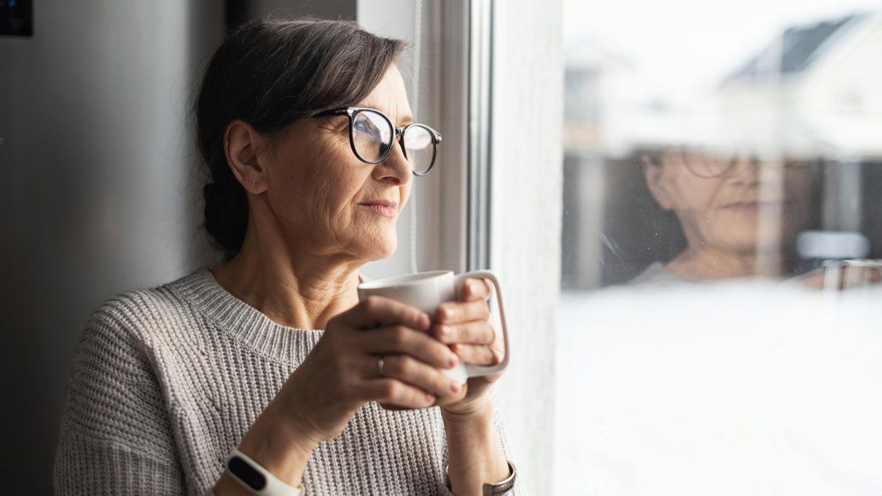 Woman holding mug of coffee looking out the window appearing to be lonely