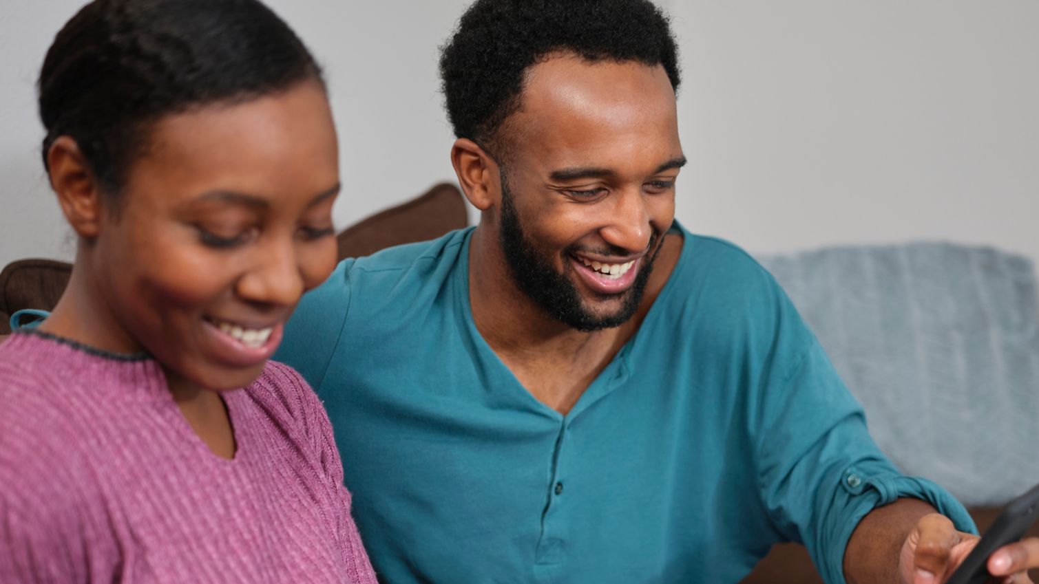 young couple looking at booklet and the phone on the couch