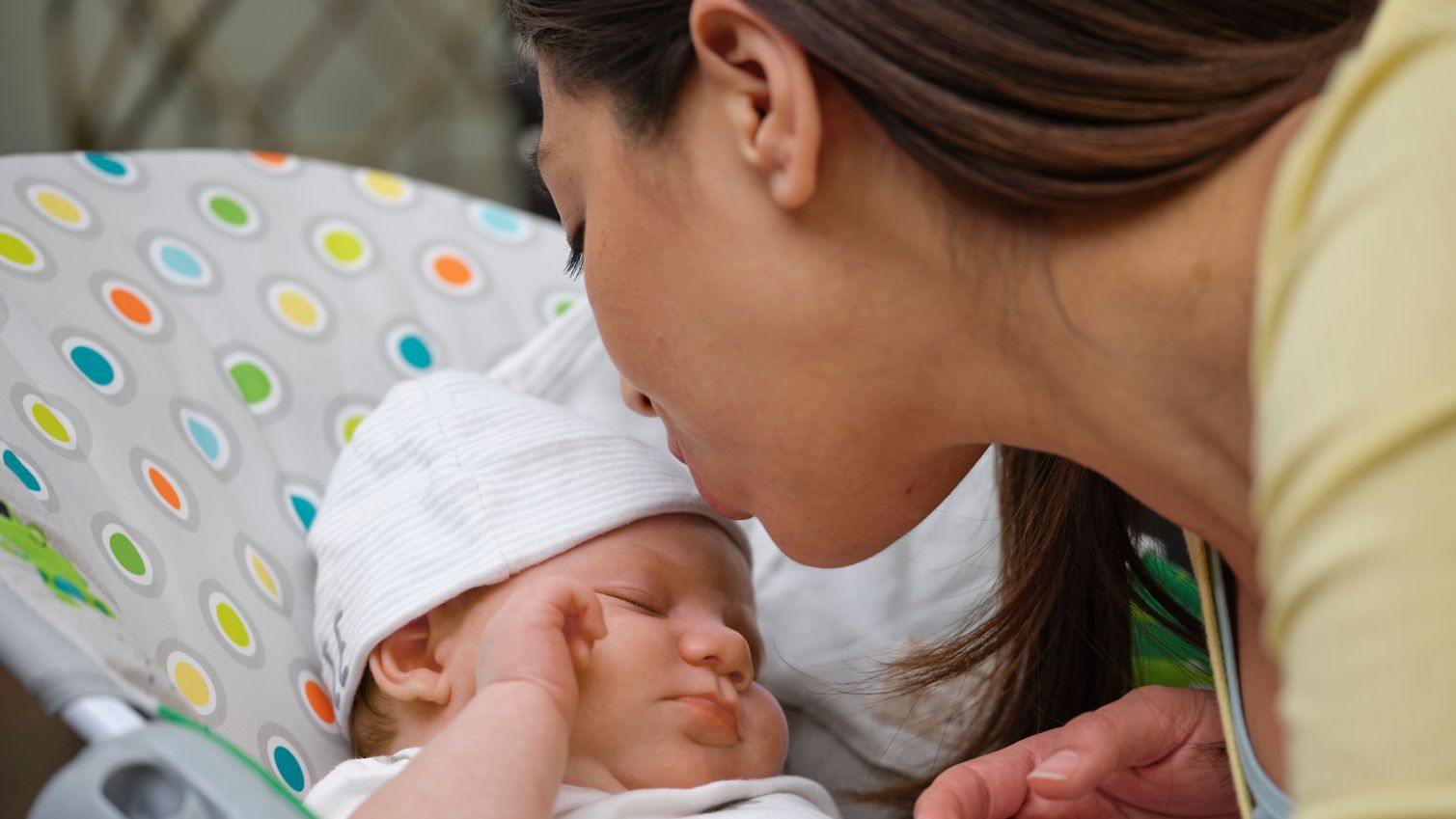 New mother kissing newborn baby in baby carrier