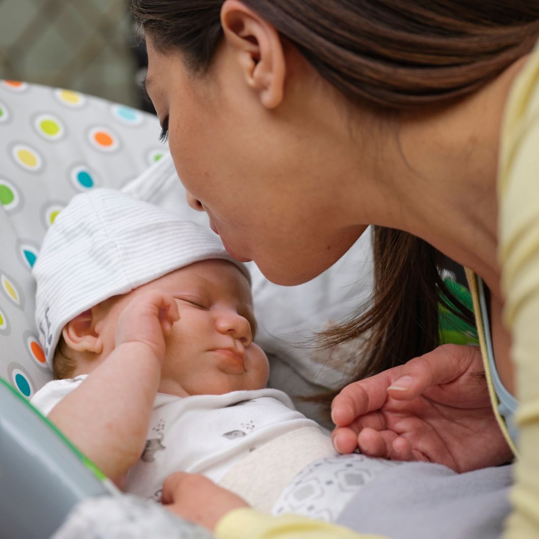 New mom kisses newborn in baby seat