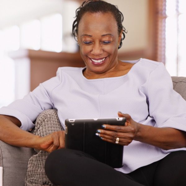 Older woman sitting on a couch with a smile, browsing on an iPad in her living room