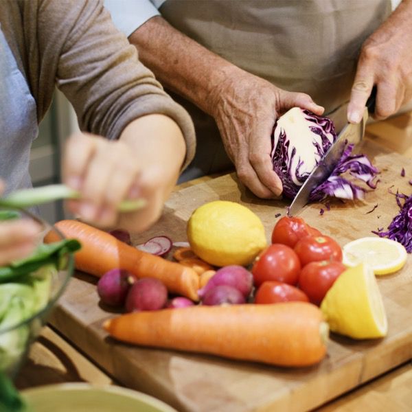 Man chopping purple lettuce with other vegetables like carrot, tomato and lemon on the side on wooden chopping board.