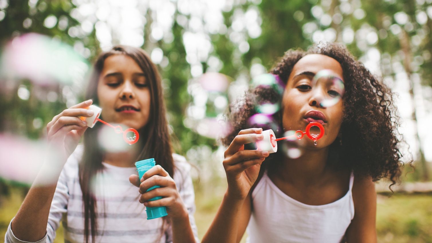 Two young girls blow bubbles outside