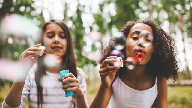 Two young girls blow bubbles outside