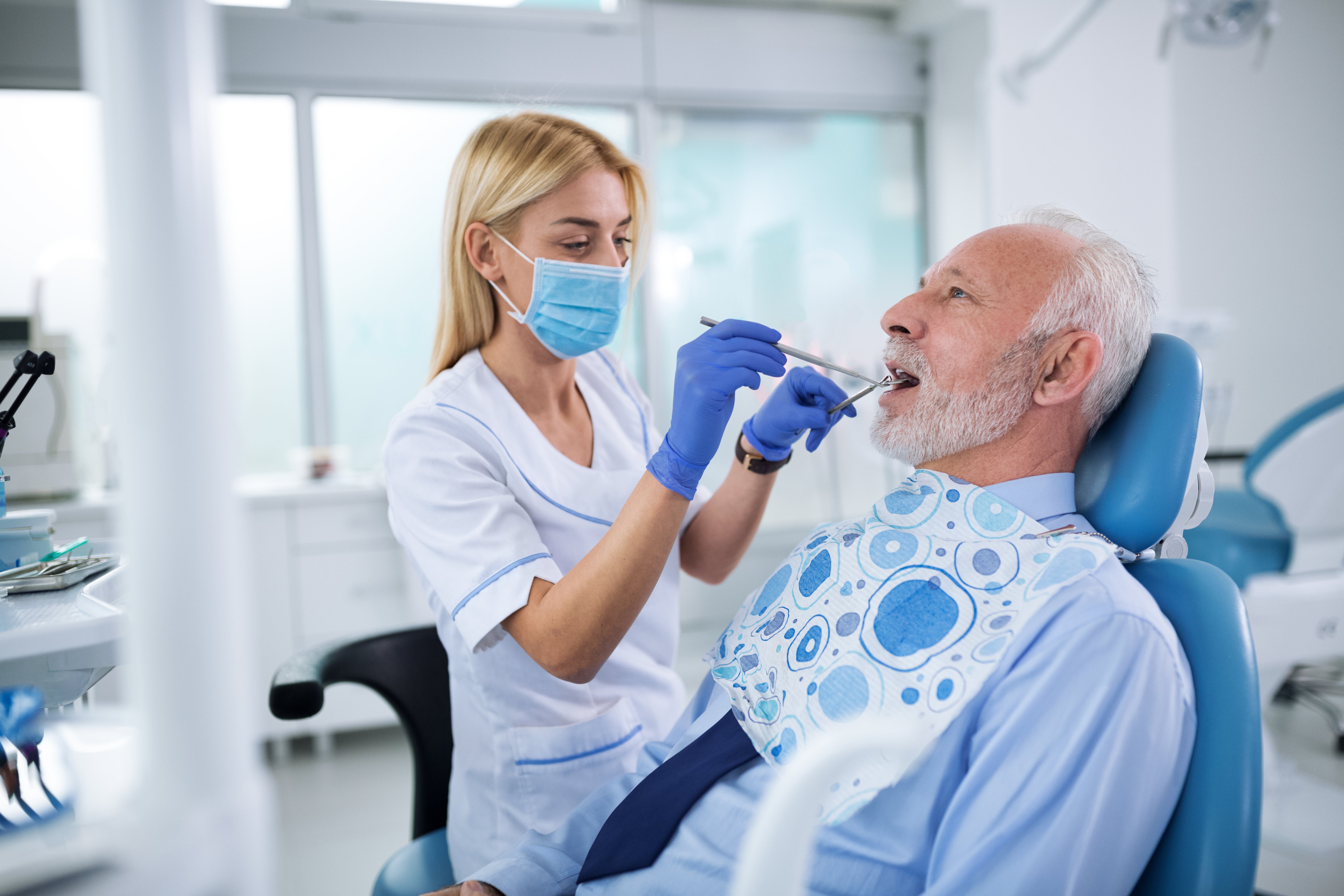Dentist with  sterile mask, protected surgical gloves and dental instruments held in the hands, examining  teeth of an elderly patient
