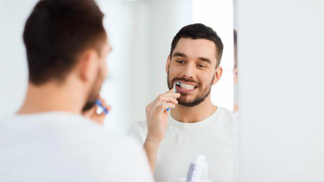 A man carefully brushes his teeth.