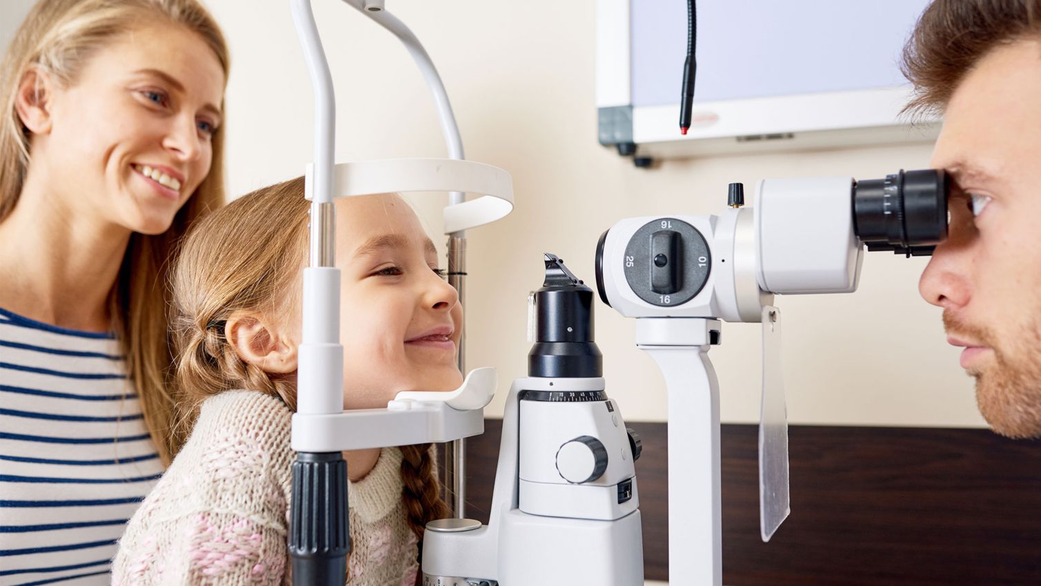 A child gets an eye exam while her mom looks on.