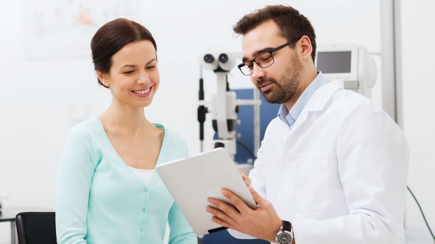 An eye doctor uses tablet while patient looks on. 
