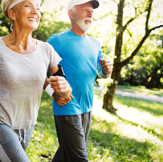 An older woman and man wearing workout gear jog together outside.