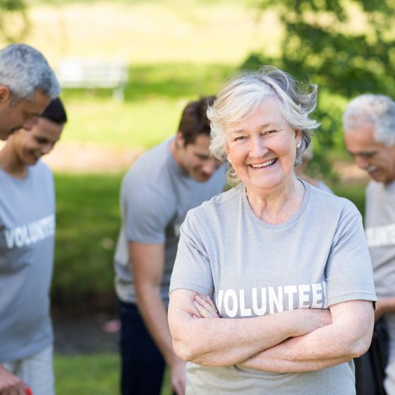 An older woman with a tee shirt that says “volunteer” smiles as she stands next to a group of other volunteers.
