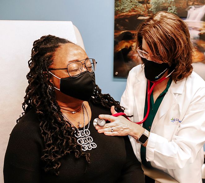 Doctor's visit where masked doctor checks on her patient with a stethoscope 