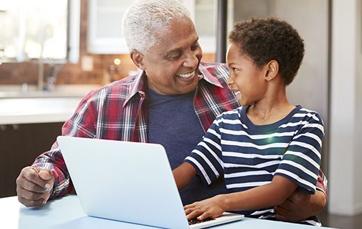 Son sitting on his grandfather's lap and typing on keyboard