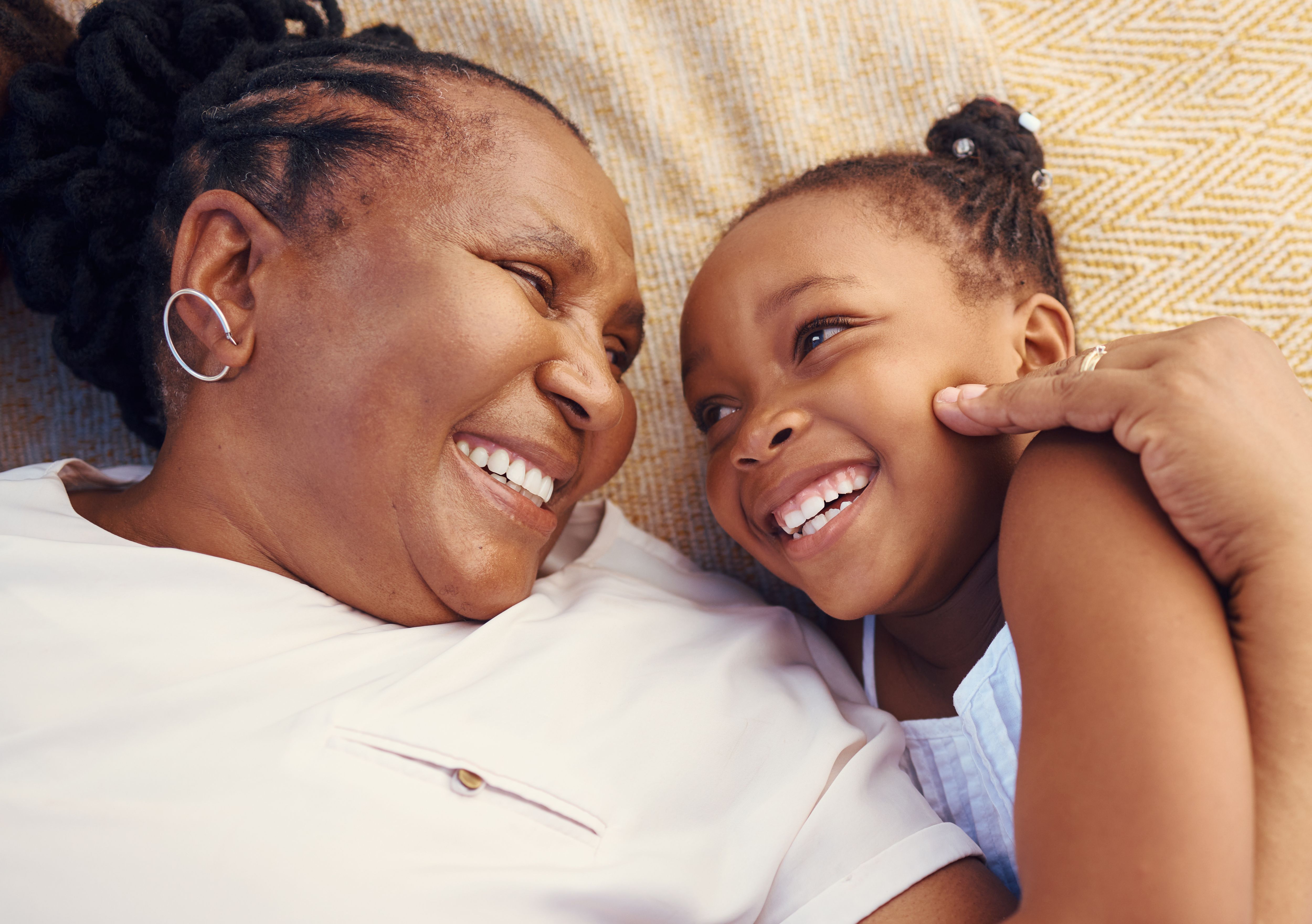 Happy, smile and family of a black grandma and child in happiness relaxing and lying on a bed at home. Senior African grandmother and little girl in joyful, love and smiling together in the bedroom.